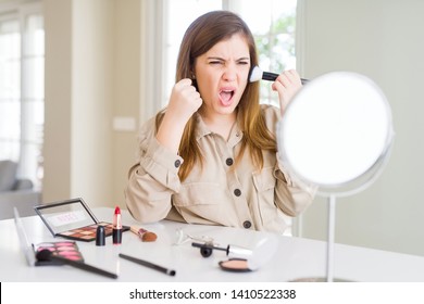 Beautiful young woman using make up cosmetics applying color using brush annoyed and frustrated shouting with anger, crazy and yelling with raised hand, anger concept