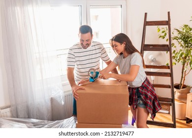 Beautiful Young Woman Using A Packing Machine, Taping Cardboard Boxes, Getting Ready For Relocation; Couple Packing Things While Moving House