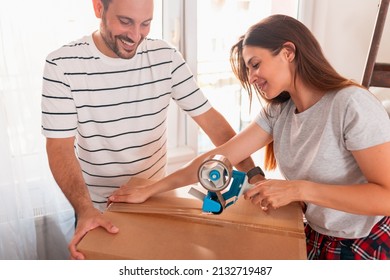 Beautiful Young Woman Using A Packing Machine, Taping Cardboard Boxes, Getting Ready For Relocation; Couple Packing Things While Moving House