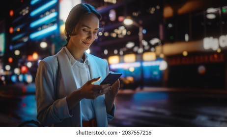 Beautiful Young Woman Using Smartphone Walking Through Night City Street Full of Neon Light. Portrait of Gorgeous Smiling Female Using Mobile Phone, Posting Social Media, Online Shopping, Texting - Powered by Shutterstock