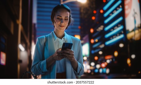 Beautiful Young Woman Using Smartphone Walking Through Night City Street Full of Neon Light. Smiling Thoughtfully Female Using Mobile Phone, Posting Social Media, Online Shopping, Texting. - Powered by Shutterstock