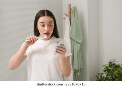 Beautiful young woman using smartphone while brushing teeth in bathroom. Internet addiction - Powered by Shutterstock