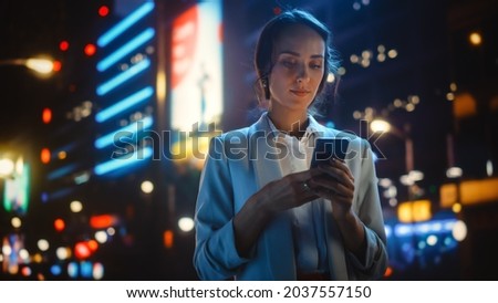 Beautiful Young Woman Using Smartphone Standing on the Night City Street Full of Neon Light. Portrait of Young Woman Holding Mobile Phone, Posting Social Media, Online Shopping, Texting.