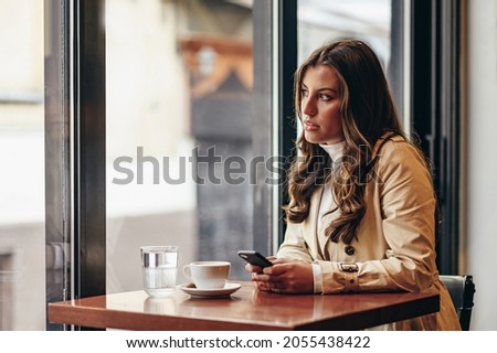Beautiful young woman using a smartphone while sitting in a coffee shop near the window