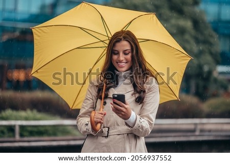 Beautiful young woman using smartphone and holding a yellow umbrella during a heavy rain in the city