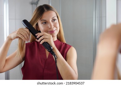 Beautiful Young Woman Using Steam Straightener To Style Hair At The Mirror On Bathroom