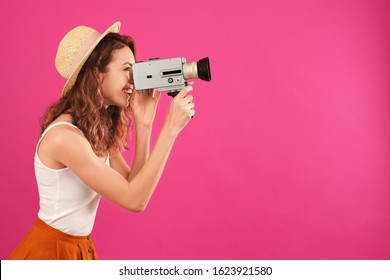 Beautiful young woman using vintage video camera on crimson background, space for text