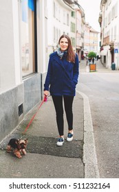 Beautiful young woman walking down the street with yorkshire terrier dog, wearing warm blue jacket