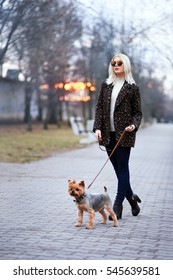 Beautiful young woman walking down the street with yorkshire terrier dog, wearing warm jacket