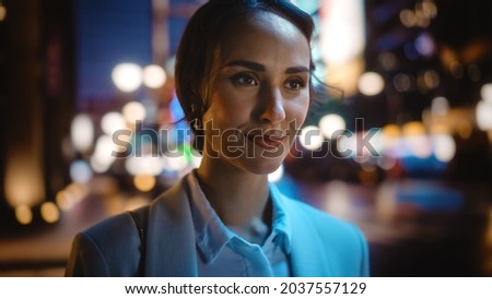 Beautiful Young Woman Walking Through Night City Street Full of Neon Lights and Entertainment Venues. Smiling Attractive Thoughtful Independent Woman Traveling. Close-up Portrait