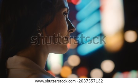 Beautiful Young Woman Walking Through Night City Street Full of Neon Lights and Entertainment Venues. Smiling Attractive Thoughtful Independent Woman Traveling. Over the Shoulder Shot.
