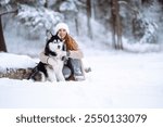 Beautiful young woman walks through the winter forest with her dog. usky dog. Pet owner enjoys walking her dog outdoors. Friendship concept, pets.