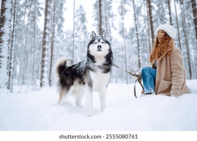 Beautiful young woman walks through the winter forest with her dog. usky dog. Pet owner enjoys walking her dog outdoors. Friendship concept, pets.