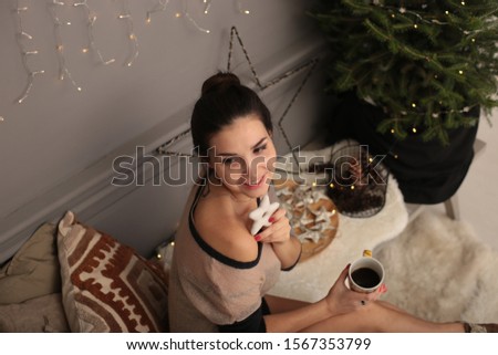 	
Beautiful young woman in a warm transparent sweater with gingerbread cookies and a cup of tea