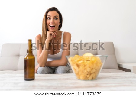 A beautiful young woman watching thrilled something on a Screen with Beer and potato Chips.
