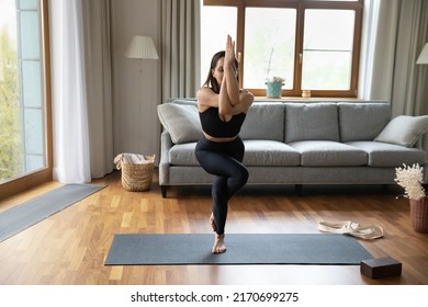 Beautiful Young Woman Wear Black Sportswear Working Out At Modern Home, Doing Advanced Yoga, Perform Eagle Asana Or Garudasana Pose, Full Length. Improves Balance, Strengthens Body, Training Concept