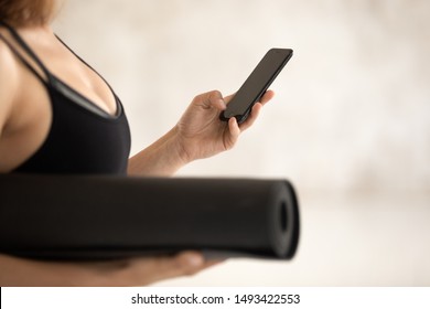 Beautiful Young Woman Wearing Black Sportswear, Fitness Instructor Holding Yoga Mat, Using Phone Close Up, Waiting For Training, Browsing Apps, Sporty Girl Looking At Empty Cellphone Screen