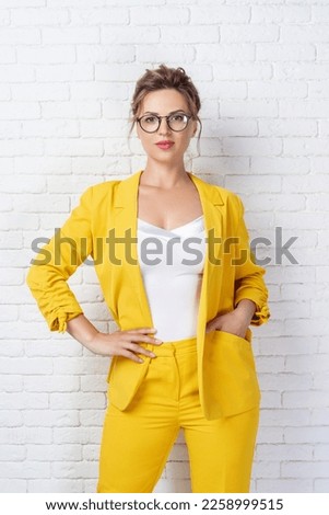 Beautiful young woman wearing a bright yellow suit and glasses. Portrait of adult woman