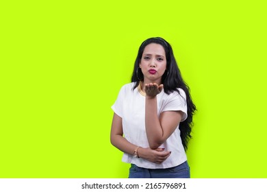 Beautiful young woman wearing casual white t shirt looking at the camera blowing kiss with hand on air being lovely and sexy isolated over green background. love expression