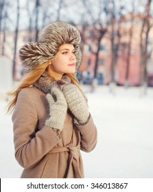 Beautiful young woman wearing a coat and hat over snow in winter day, profile view