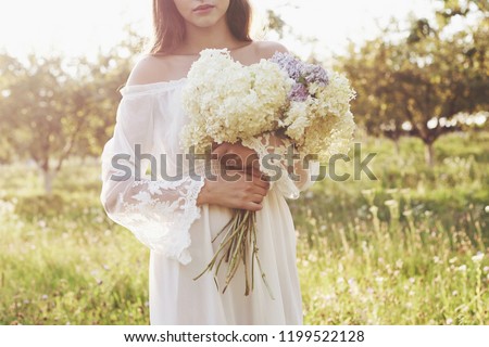 Beautiful young woman wearing elegant white dress and enjoying beautiful sunny afternoon in a summer garden.