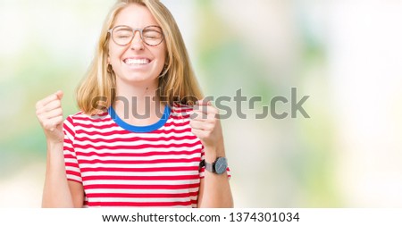 Beautiful young woman wearing glasses over isolated background excited for success with arms raised celebrating victory smiling. Winner concept.