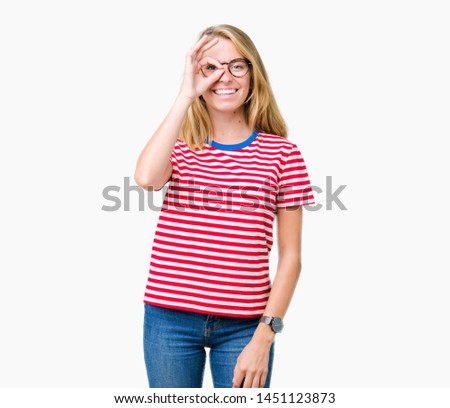 Beautiful young woman wearing glasses over isolated background doing ok gesture with hand smiling, eye looking through fingers with happy face.