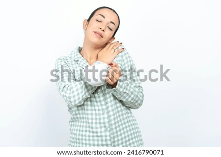Beautiful young woman wearing green plaid pajama Hugging oneself happy and positive, smiling confident. Self love and self care