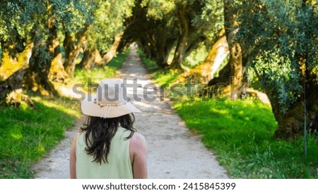 Beautiful young woman wearing a hat standing on a road in the forest with rays of sunlight beaming through the leaves of the trees