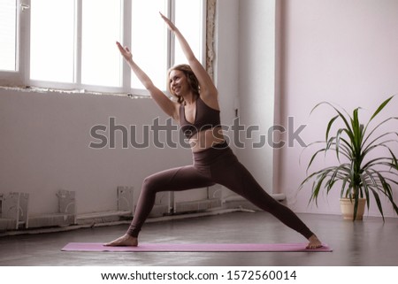 Beautiful young woman wearing jumpsuit working out against vintage window, doing yoga or pilates exercise