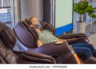 Beautiful young woman wearing a medical mask due to the coronavirus COVID 19 relaxing on the massage chair in airport or in the mall