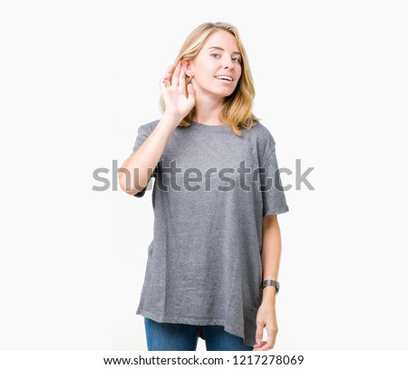 Beautiful young woman wearing oversize casual t-shirt over isolated background smiling with hand over ear listening an hearing to rumor or gossip. Deafness concept.
