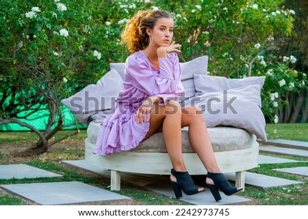 Beautiful young woman wearing a purple dress at a garden. Beautiful woman on a flourish garden on spring time. Sunny day.