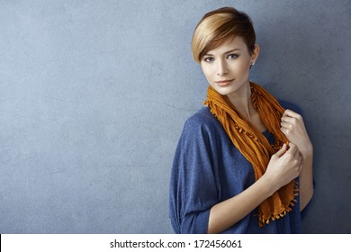 Beautiful young woman wearing scarf standing by grey wall, looking at camera. Copy space.