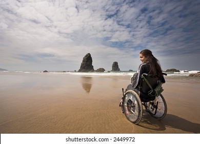 Beautiful Young Woman In A Wheel Chair Visiting Cannon Beach In Oregon, USA.