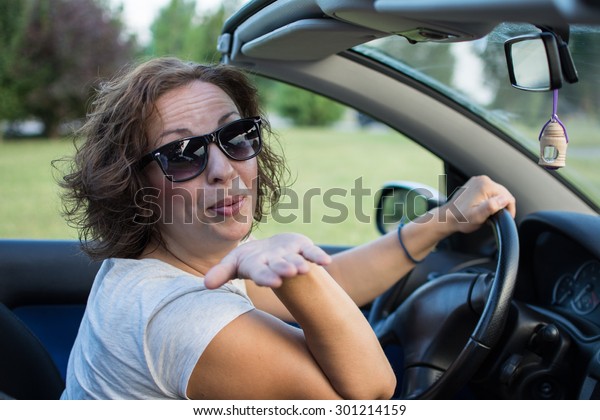 Beautiful young woman in white shirt\
and black glasses, smiling from a car and giving a\
kiss