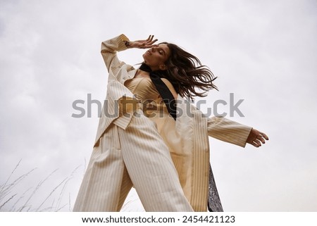 A beautiful young woman in a white suit and black tie, embracing the summer breeze in a field of nature.