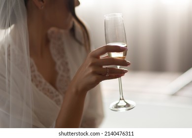 Beautiful Young Woman In White Wedding Robe Holding Champagne Glass In Hand. Bridal Morning. The Bride Is Drinking Champagne In A Hotel Room. 