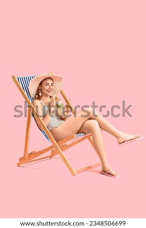 Beautiful young woman in wicker hat with glass of tasty mojito sitting on deckchair against pink background