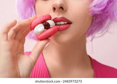 Beautiful young woman in wig with sweet macaroon on pink background