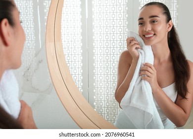 Beautiful Young Woman Wiping Face With Towel Near Mirror In Bathroom. Facial Wash