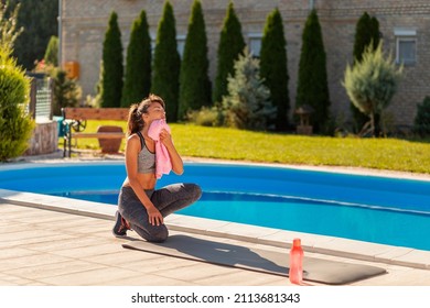 Beautiful Young Woman Wiping Sweat Using A Towel After An Outdoor Workout In Her Backyard By The Swimming Pool