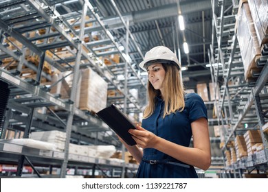 Beautiful young woman worker of furniture store in shopping center. Girl looking for goods with a tablet is checking inventory levels in a warehouse. Logistics concept