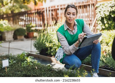 Beautiful young woman working at a greenhouse and writing on a tablet clipboard. - Powered by Shutterstock