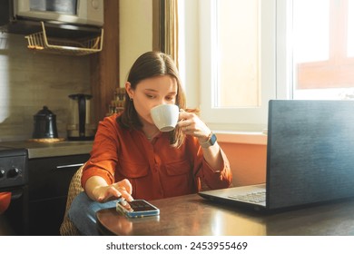 Beautiful young woman working at the kitchen table with a cup of coffee. Business woman working with a laptop and calculator. Home office, work from home, self-employment. - Powered by Shutterstock