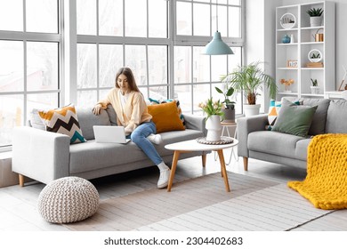 Beautiful young woman working with laptop on cozy sofa near big window - Powered by Shutterstock