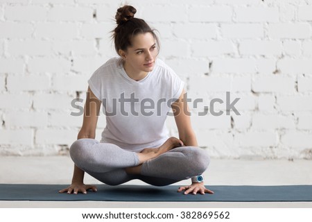 Beautiful young woman working out in loft interior, doing yoga exercise on blue mat, arm balance exercise with crossed legs, Scale Posture, Tolasana, Utpluthi Pose, full length
