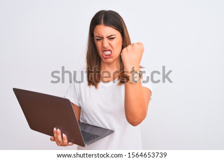 Beautiful young woman working using computer laptop over white background angry and mad raising fist frustrated and furious while shouting with anger. Rage and aggressive concept.