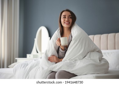 Beautiful Young Woman Wrapped With Soft Blanket Holding Cup Of Hot Drink On Bed At Home