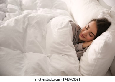 Beautiful young woman wrapped with soft blanket sleeping in bed at home